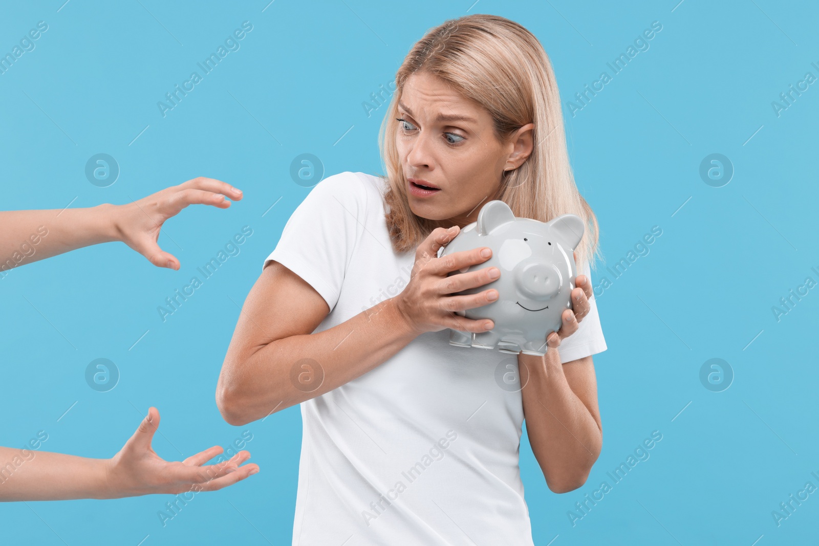 Photo of Scammer taking piggy bank from scared woman on light blue background. Be careful - fraud