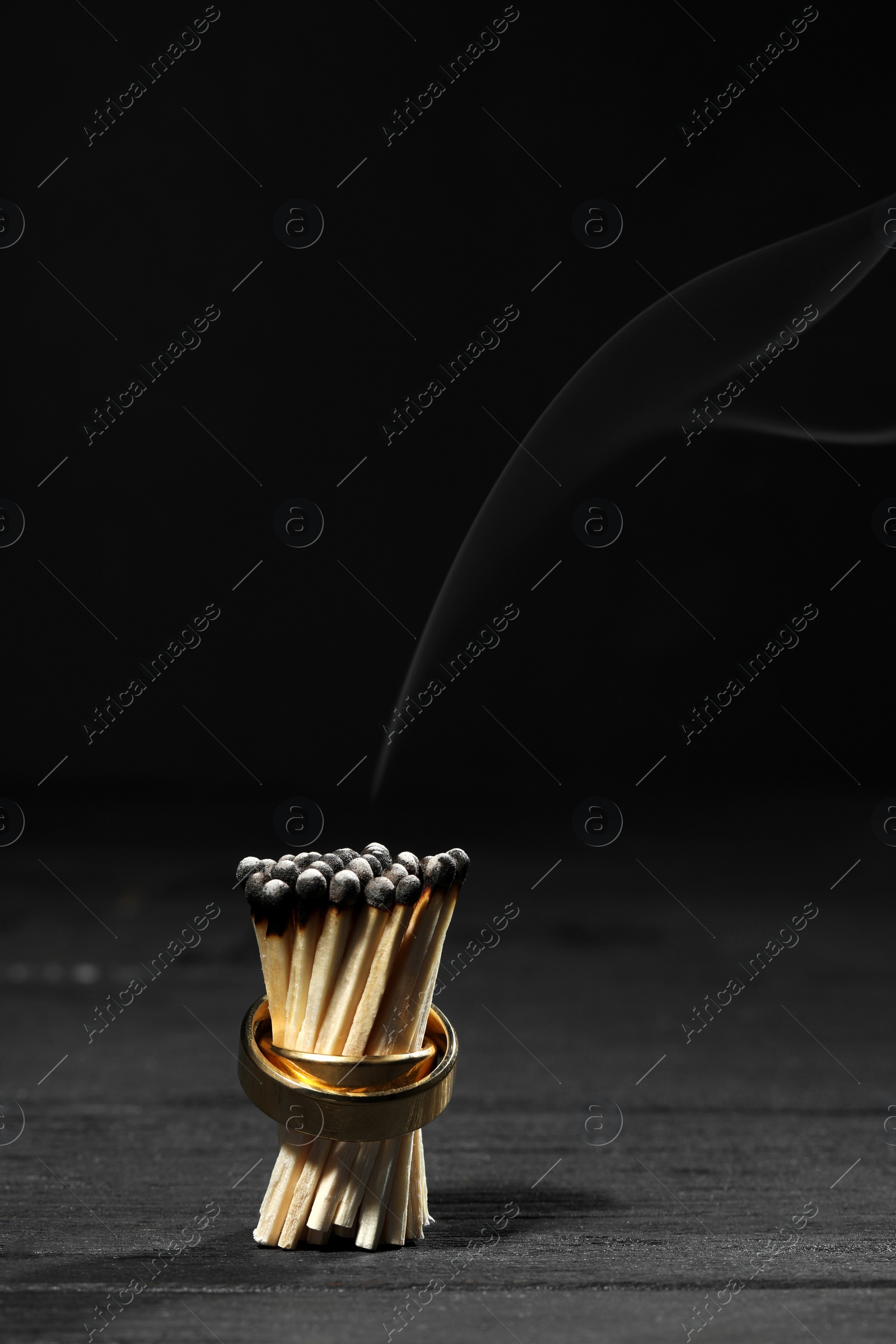 Photo of Burnt matches with gold wedding rings on black background, space for text. Divorce concept