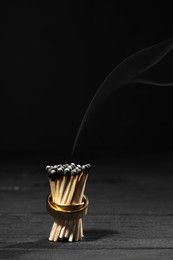 Photo of Burnt matches with gold wedding rings on black background, space for text. Divorce concept