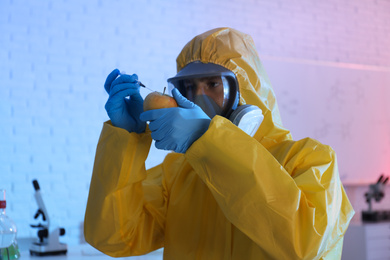 Scientist in chemical protective suit injecting apple at laboratory