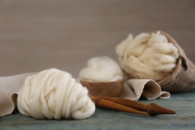 Photo of Soft white wool and spindles on blue wooden table. Space for text