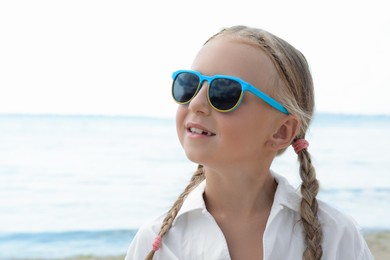 Little girl wearing sunglasses at beach on sunny day. Space for text