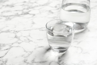 Photo of Glass and jug with fresh water on marble table. Space for text