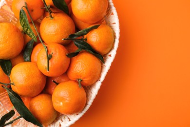 Photo of Fresh ripe tangerines and leaves in basket on orange table, top view. Space for text