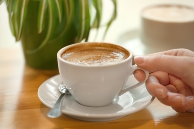 Photo of Woman with cup of aromatic coffee at wooden table