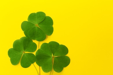 Photo of Beautiful green four leaves clover on yellow background, top view. Space for text