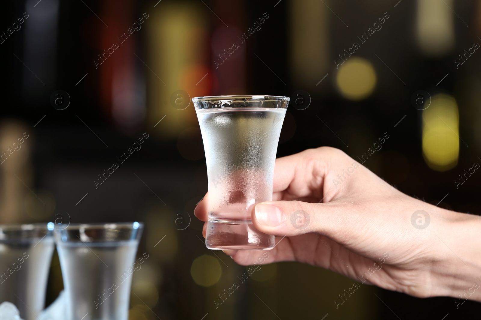 Photo of Woman holding shot of vodka on blurred background, closeup