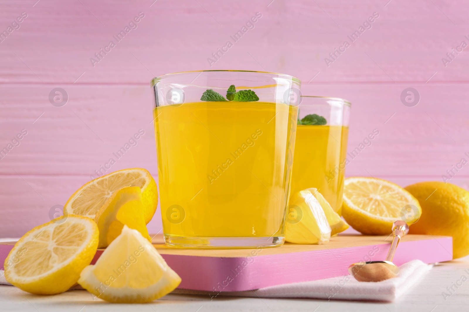 Photo of Glasses of lemon jelly served on light wooden table against color background