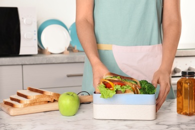 Photo of Woman packing food for her child at table in kitchen, closeup. Healthy school lunch