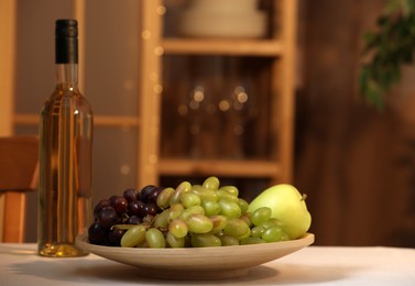 Photo of Bottle of wine and plate with ripe fruits on table indoors