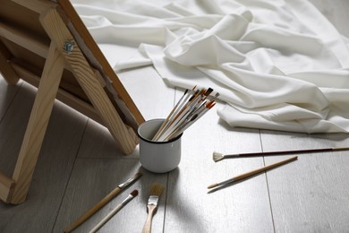 Photo of Different brushes near stand with canvas on floor in artist's studio