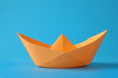Photo of Handmade orange paper boat on light blue background. Origami art