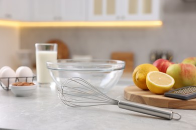 Metal whisk, bowl, grater and different products on gray marble table in kitchen