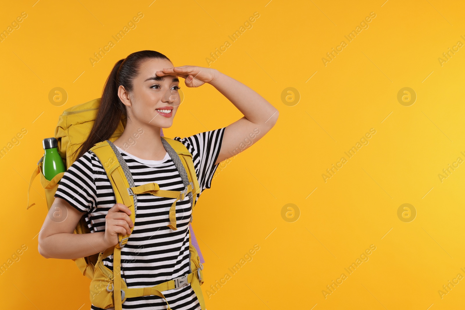 Photo of Smiling young woman with backpack on orange background, space for text. Active tourism