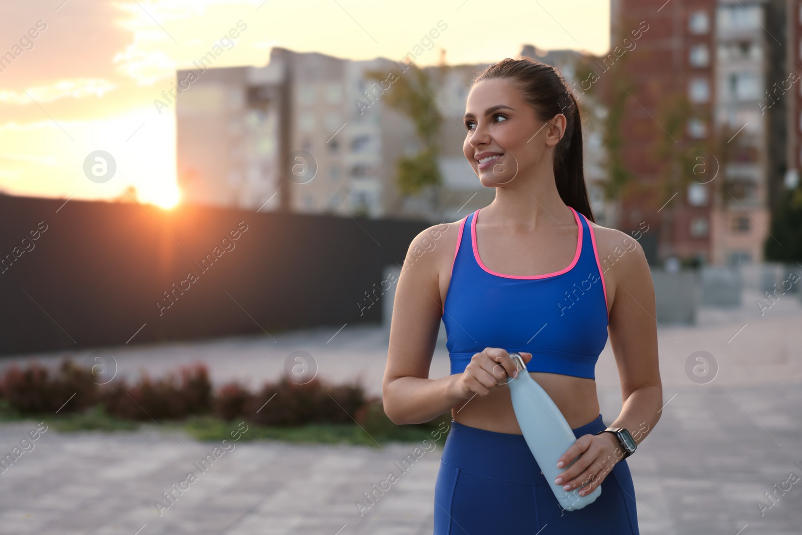 Photo of Beautiful woman in stylish sportswear with bottle of drink on city street, space for text