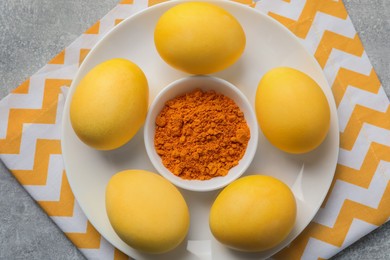 Yellow Easter eggs painted with natural dye and turmeric powder in bowl on light gray textured table, top view