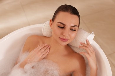 Photo of Young woman using pillow while enjoying bubble bath indoors, above view