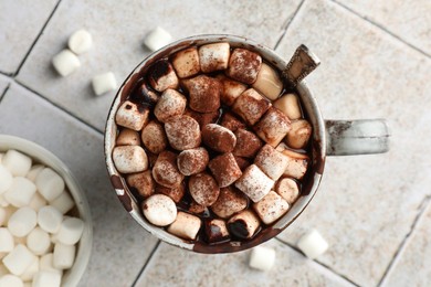 Photo of Delicious hot chocolate with marshmallows, cocoa powder and spoon in cup on tiled table, top view