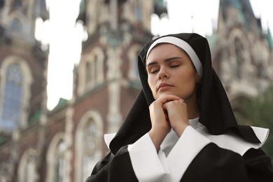 Photo of Young nun with hands clasped together while praying near cathedral outdoors, space for text