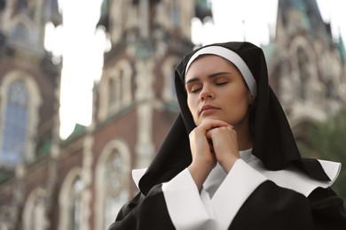 Young nun with hands clasped together while praying near cathedral outdoors, space for text