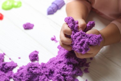 Photo of Little child playing with kinetic sand at white wooden table, closeup