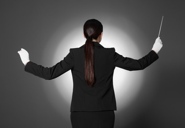 Professional conductor with baton on grey background, back view