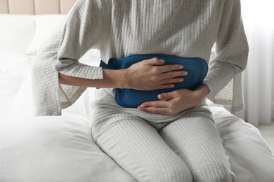 Photo of Woman using hot water bottle to relieve abdominal pain on bed at home, closeup