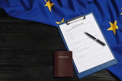 Photo of Visa application form, passport, pen and flag of European Union on black wooden table, flat lay. Space for text