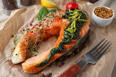 Photo of Tasty salmon with spinach on parchment, closeup