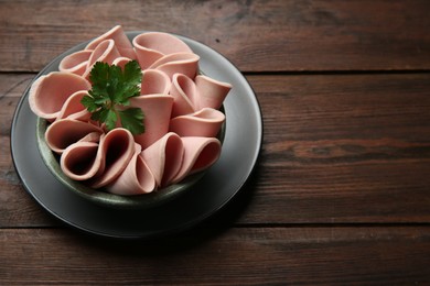 Slices of delicious boiled sausage with parsley on wooden table, above view. Space for text