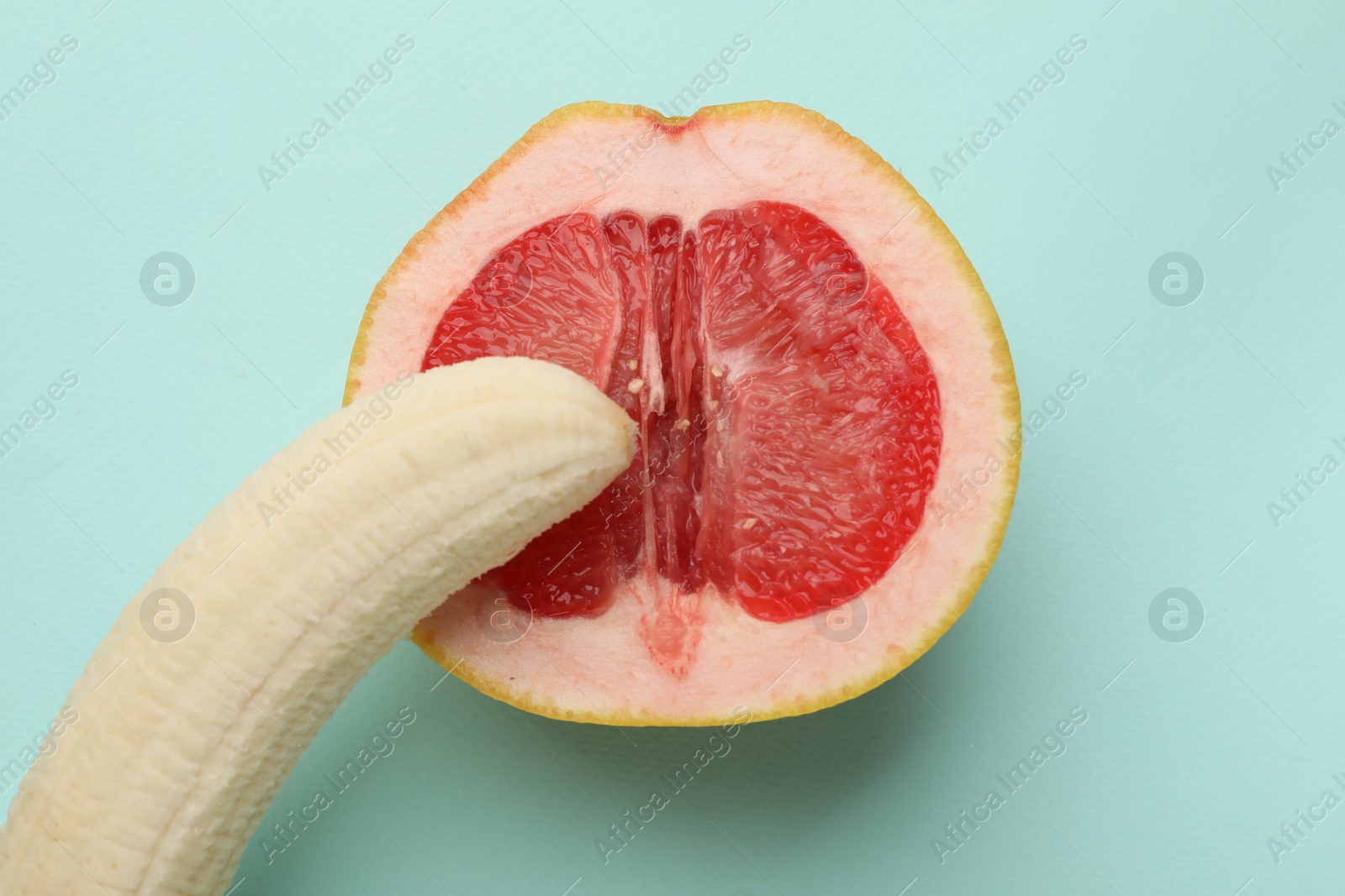 Photo of Banana and half of grapefruit on turquoise background, top view. Sex concept