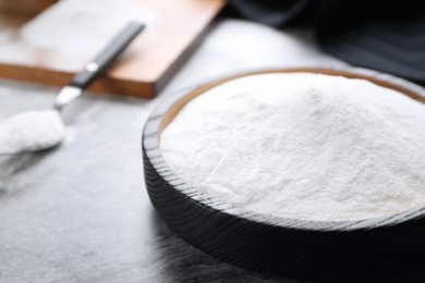 Photo of Baking soda in wooden plate on grey table, closeup