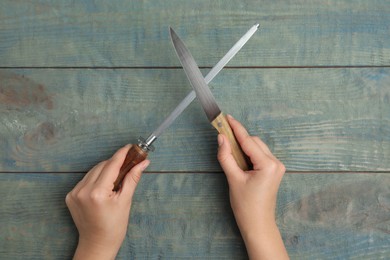 Photo of Woman sharpening knife at light blue wooden table, top view