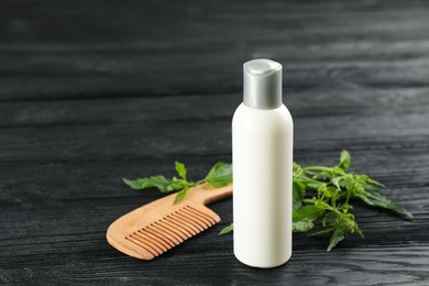 Photo of Stinging nettle, cosmetic product and comb on black wooden background. Natural hair care