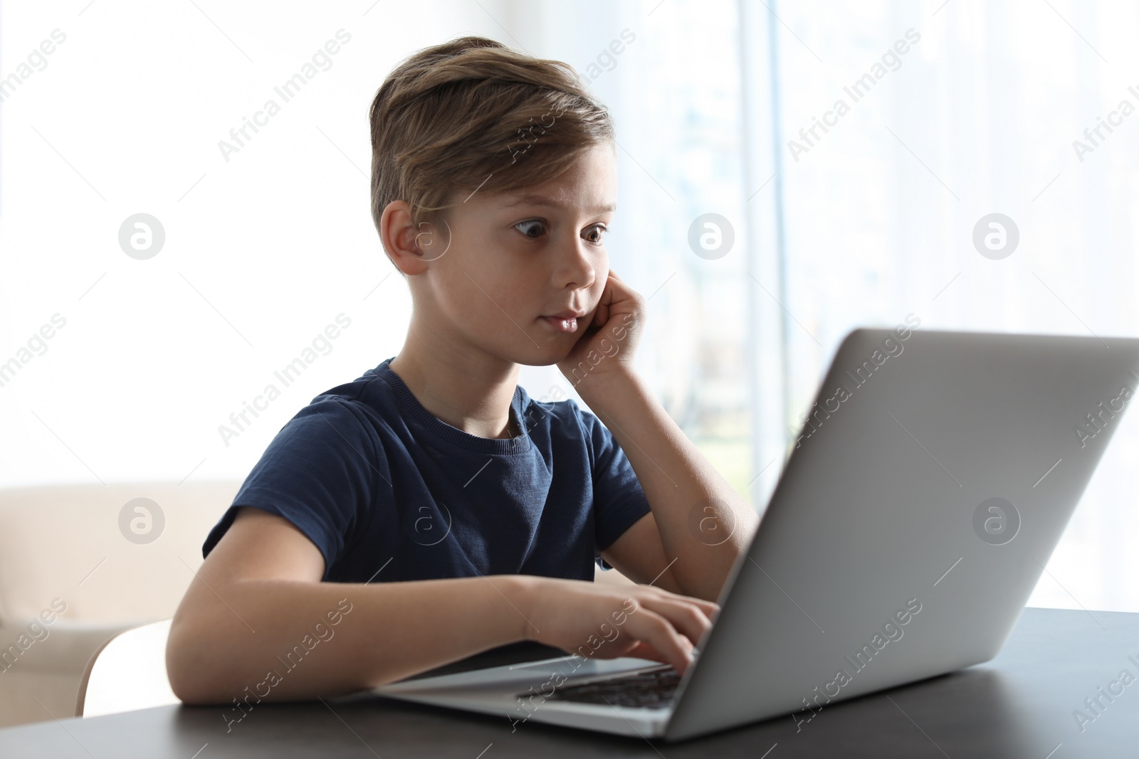 Photo of Shocked little child with laptop at table indoors. Danger of internet