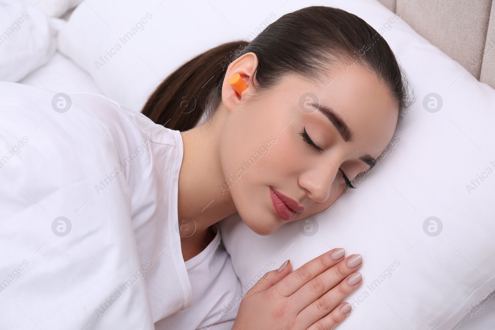 Photo of Young woman with foam ear plugs sleeping in bed