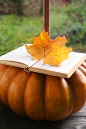 Book with autumn leaf as bookmark and ripe pumpkin on table