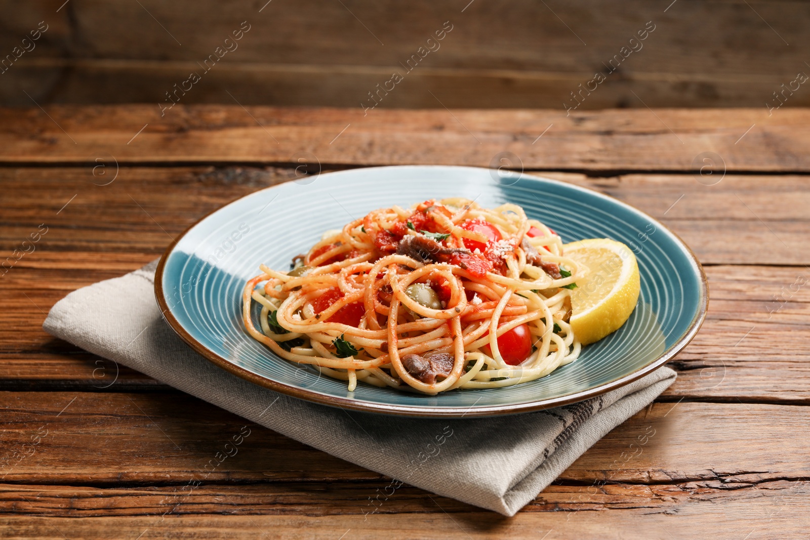 Photo of Delicious pasta with anchovies, tomatoes and parmesan cheese on wooden table