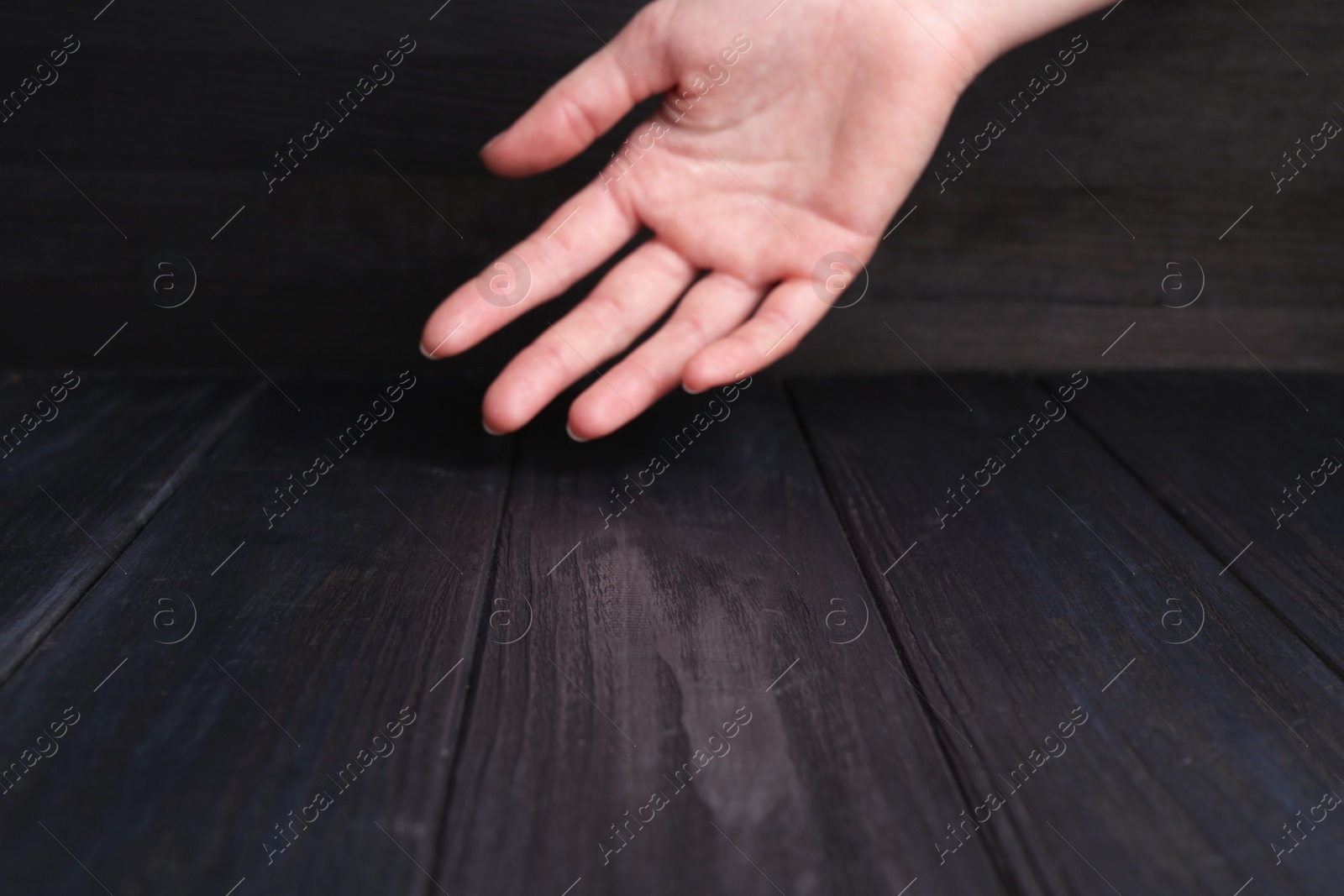 Photo of Woman holding hand above black wooden table, selective focus. Space for text