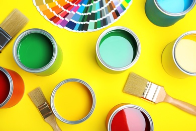 Flat lay composition with paint cans, brushes and color palette on yellow background