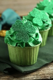 Photo of St. Patrick's day party. Tasty cupcakes with clover leaf toppers and green cream on wooden table, closeup
