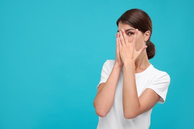 Embarrassed woman covering mouth with hands on light blue background, space for text