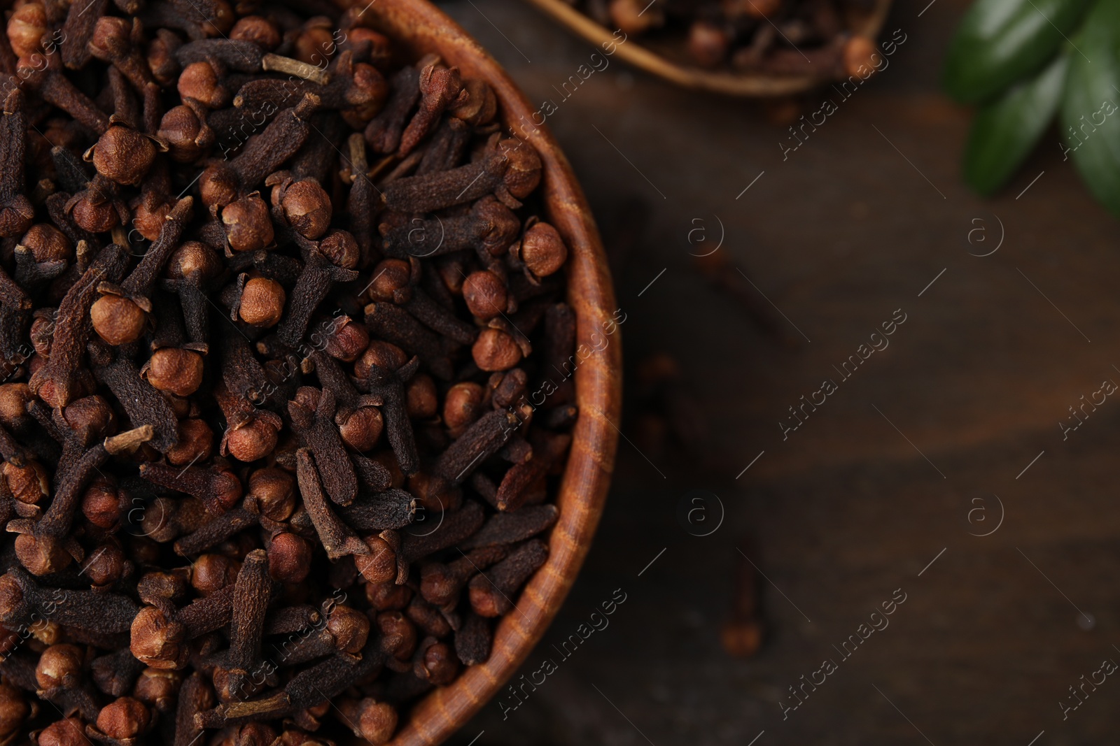 Photo of Aromatic cloves in bowl on wooden table, top view. Space for text