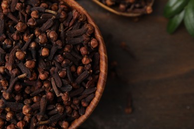 Photo of Aromatic cloves in bowl on wooden table, top view. Space for text