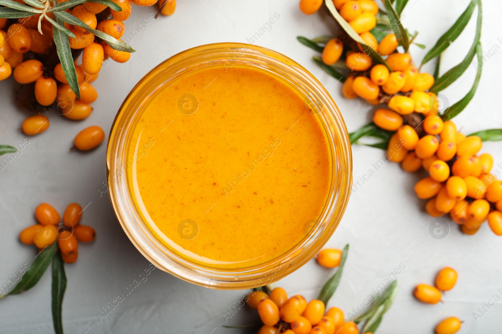 Photo of Delicious sea buckthorn jam and fresh berries on light grey table, flat lay