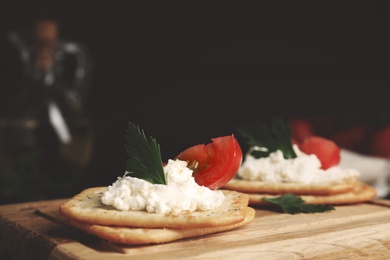 Delicious crackers with cream cheese, tomato and parsley on wooden board, closeup