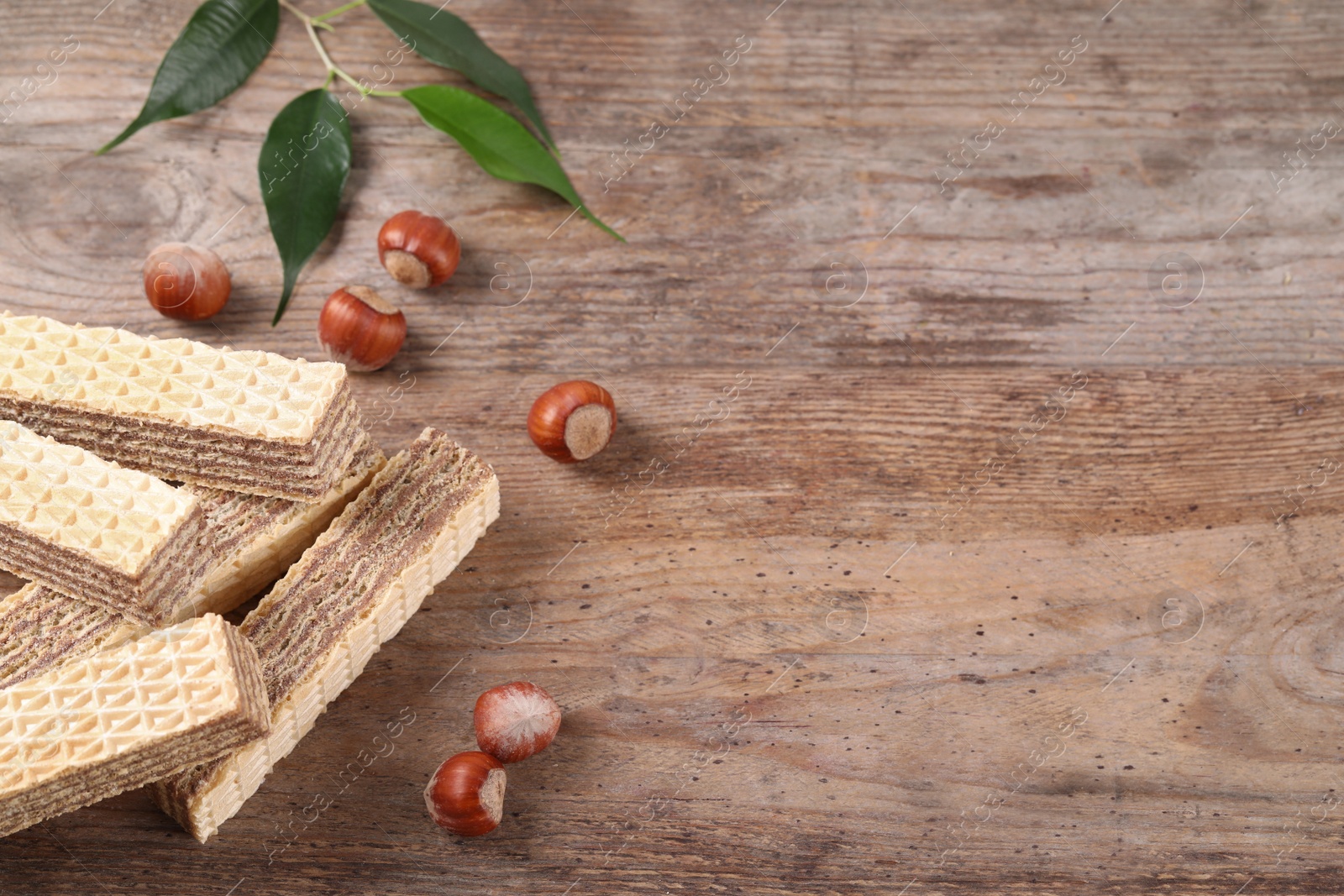 Photo of Delicious wafers with hazelnuts on brown wooden background. Space for text