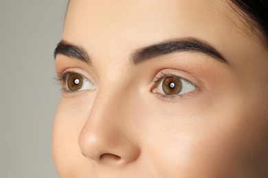 Young woman with beautiful eyebrows on grey background, closeup