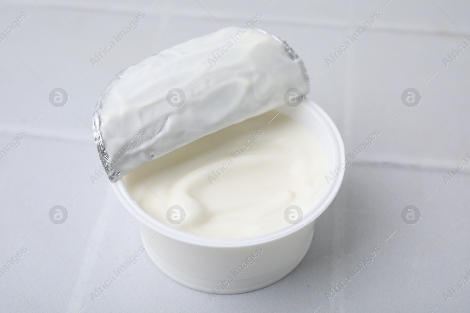 Photo of Delicious natural yogurt in plastic cup on white tiled table, closeup