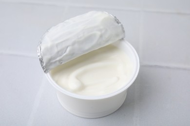 Delicious natural yogurt in plastic cup on white tiled table, closeup